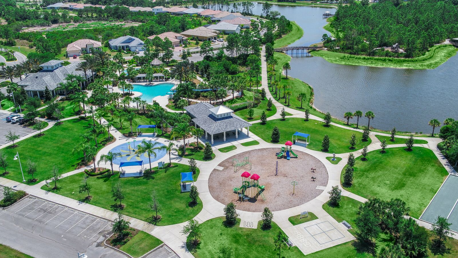 Aerial view of amenity center design featuring a clubhouse, pool, splash pad, playground, and pavilion connected by winding walkways through manicured lawns in a Florida residential community