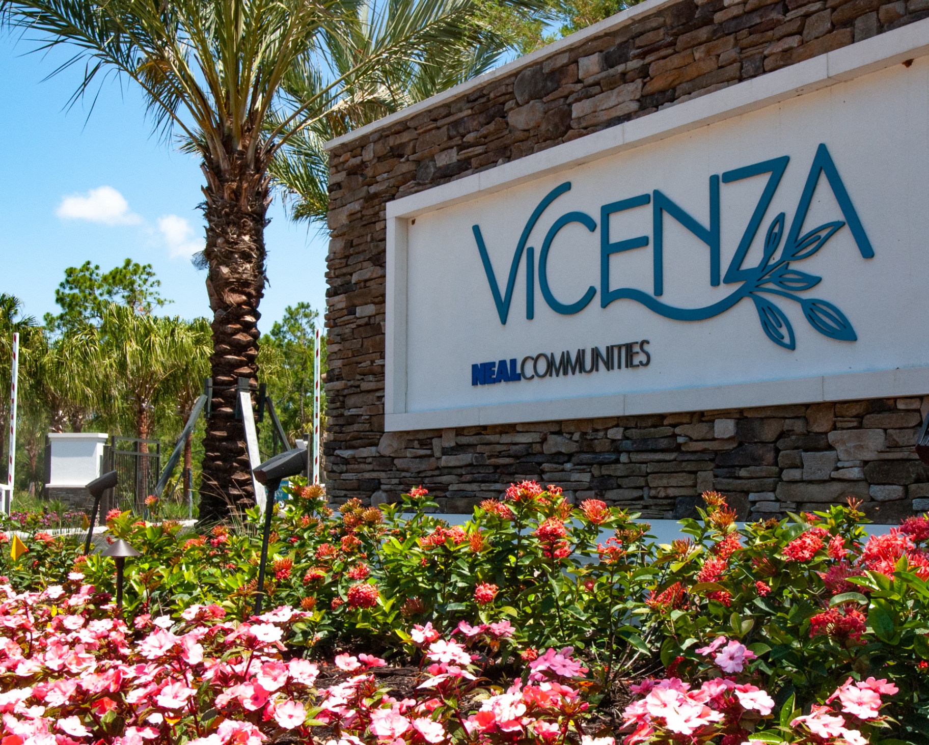 Vicenza by Neal Communities — stone-clad entry monument sign with tropical landscape and flowering groundcover