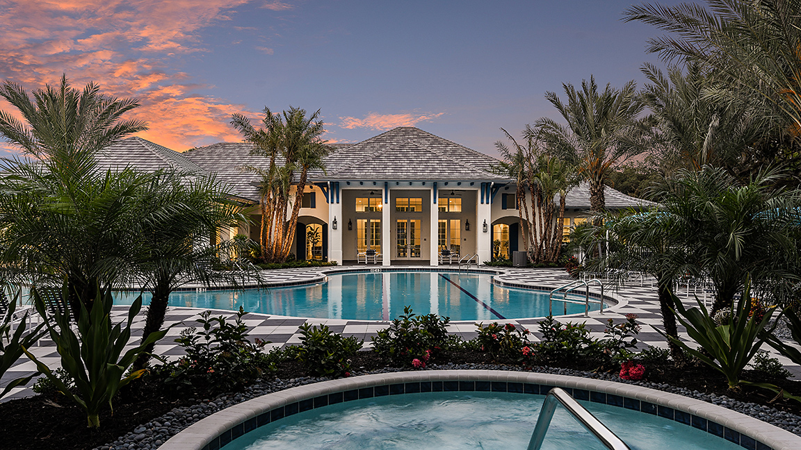 Grand Palm social club at dusk with resort pool, spa, palm trees, and illuminated clubhouse arches