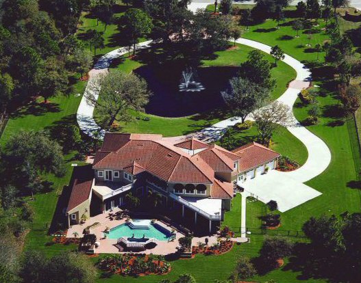 Aerial of private Florida estate with pool, lake feature, and circular drive framed by mature landscape