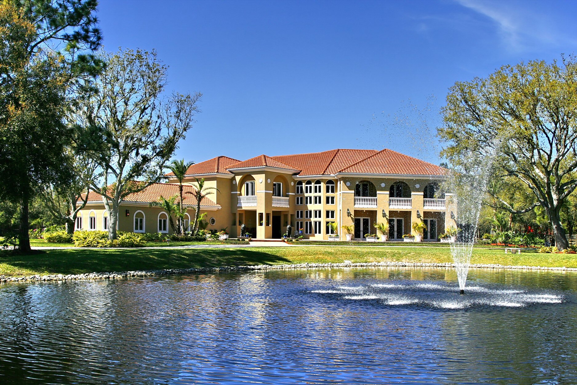 Mediterranean-style private residence with tile roof, palm landscape, and lakefront fountain