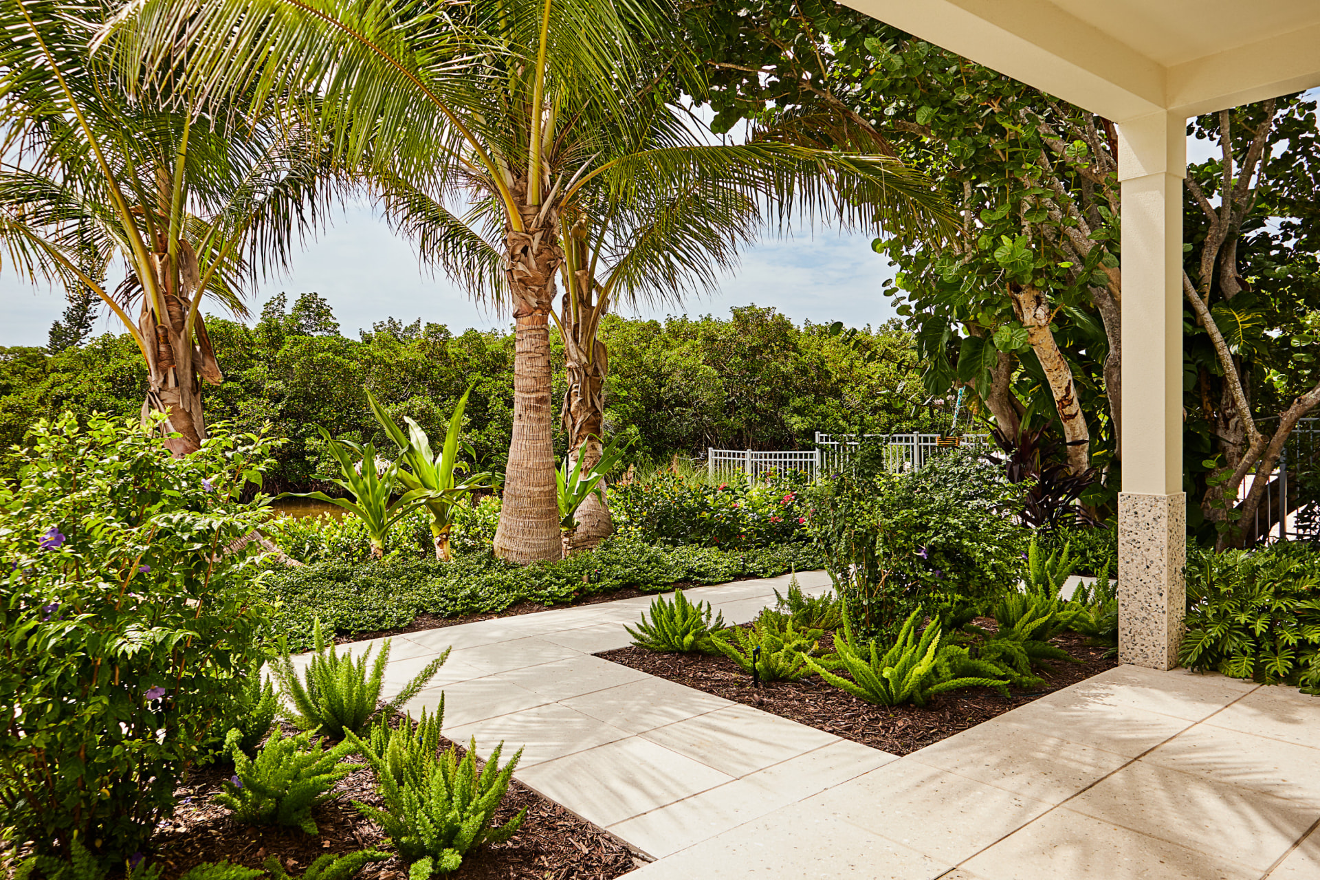 Hurricane-proof landscape design featuring storm-resilient coastal palms, deep-rooted tropical foliage, and stone walkways at a Florida residence